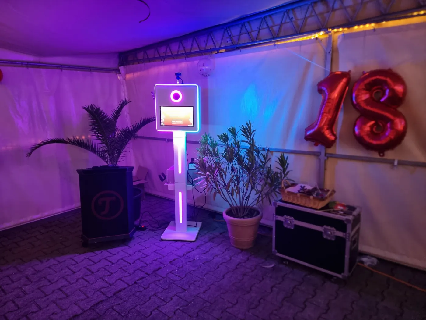 Fotobox im Festzelt mit lila Licht, Palmen und roten Ballons in Form einer 18