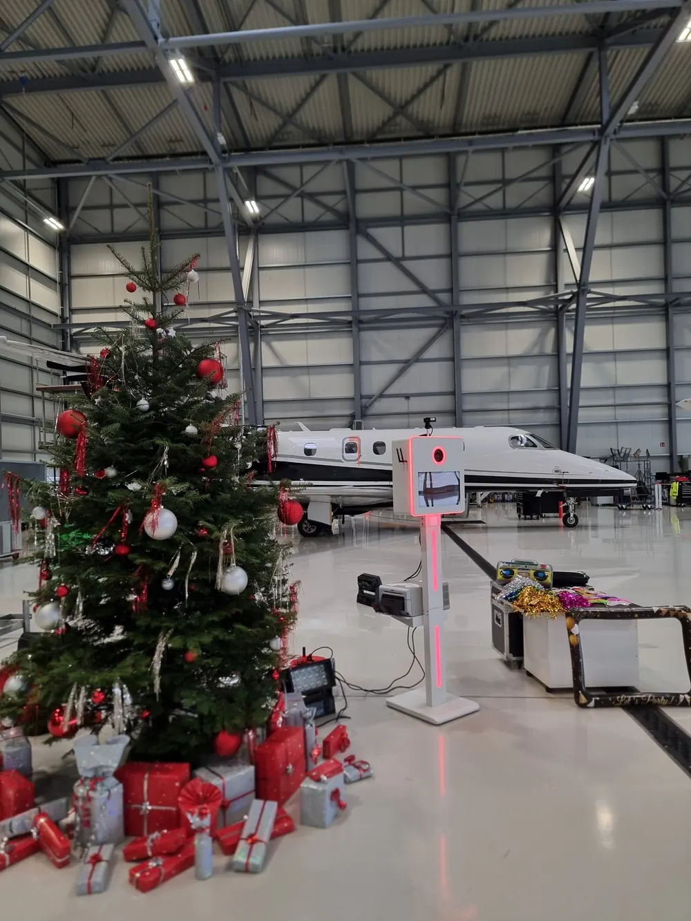 Fotobox mit roter Beleuchtung neben Weihnachtsbaum und Jet im Flugzeughangar